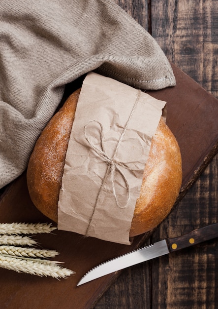 Pane appena sfornato con asciugamano da cucina e coltello sul tagliere di legno