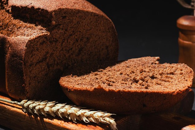 Freshly baked brown rye bread sliced ââon wooden cutting board on black background