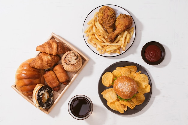 Freshly baked buns, big hamburger, fried crispy chicken and french fries on white table - Unhealthy food concept