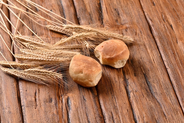 Freshly baked buns and ears of wheat on a wooden table