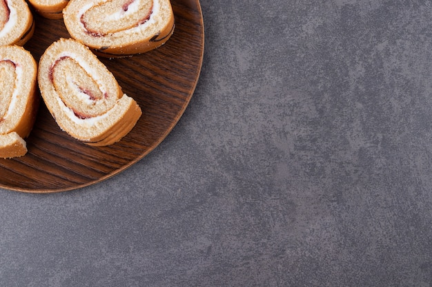 Freshly baked cake rolls on wooden plate over grey background. 