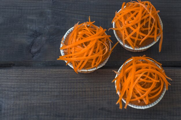 Muffin di carota di recente al forno decorati con i chip di carota freschi su fondo di legno. festa nazionale della torta di carote.