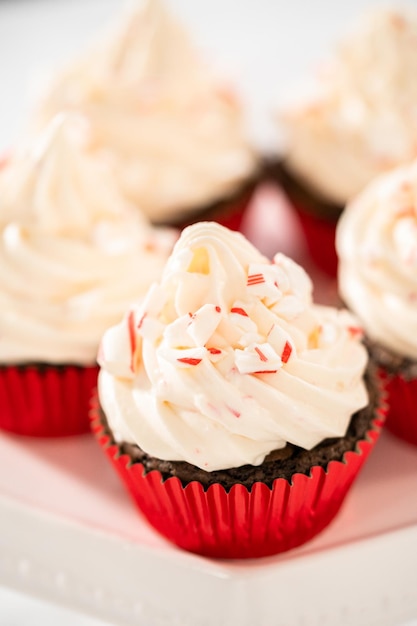 Freshly baked chocolate cupcakes with peppermint frosting and decorating with crushed peppermint candy cane candies.