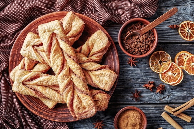 Freshly baked Cinnamon sugar puff pastry twists on a plate on a wooden rustic table, horizontal view from above, flat lay, close-up