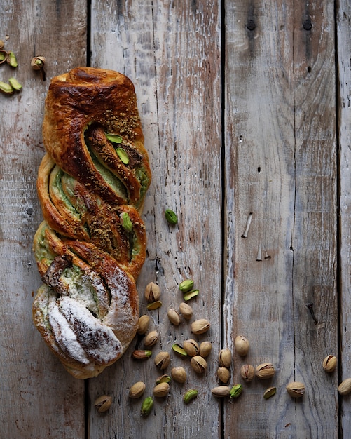 Freshly baked Cinnamon sweet bun with pistachio cream and pistachio on rustic wooden table, top view