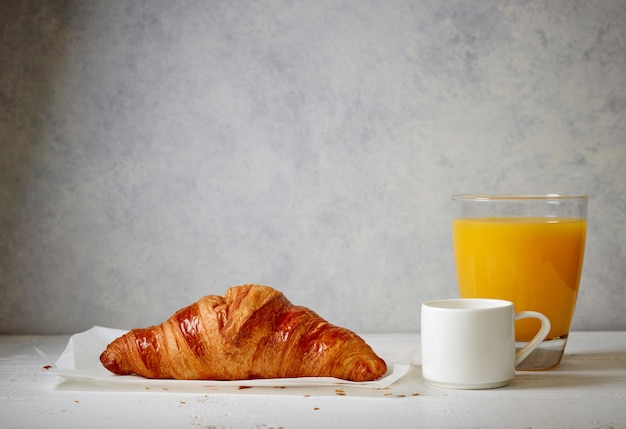 Caffè espresso croissant appena sfornato e succo d'arancia su tavola di legno bianca