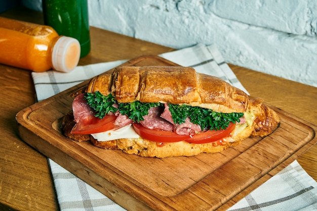 Panino croissant appena sfornato con formaggio, salame, pomodori e lattuga su una tavola di legno. cibo piatto disteso. gustosa colazione