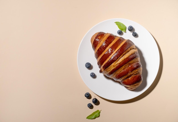 Freshly baked croissant on a white plate and blueberries on a yellow background The concept of a delicious homemade breakfast Top view and copy space