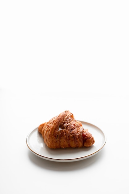 Freshly baked croissant with caramel filling on plate on white surface