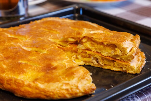 Freshly baked domestic ossetian pie on a baking sheet with cutted piece over close view