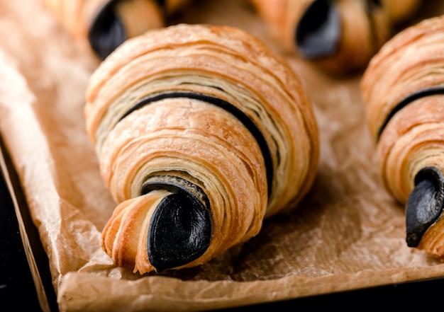 Freshly baked flaky croissants with chocolate on black metal tray on parchment