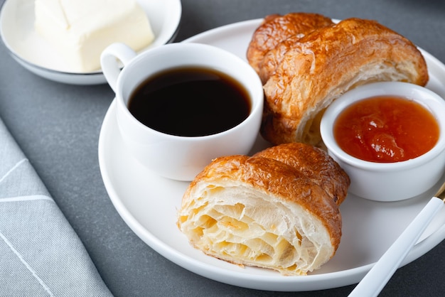 Un croissant francese appena sfornato caffè burro e marmellata colazione continentale su un tavolo grigio