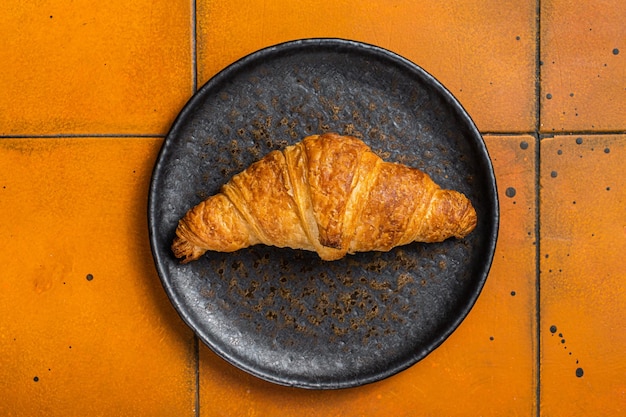 Freshly baked french croissant on a plate Orange background Top view