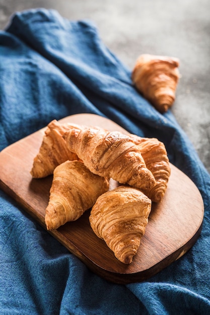 Cornetti francesi appena sfornati su una tavola di legno su un tavolo luminoso con un tovagliolo blu.