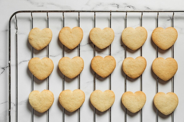 Freshly baked heart shaped shortbread cookies cooling down on a cooling rack on marble background baking for st valentine's day present top view