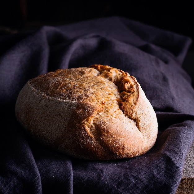 Pane di pasta acida fatto in casa appena sfornato sul tovagliolo di lino scuro, in legno.