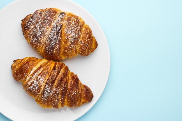 Freshly baked italian croissants on a white plate on the blue wall with copy space. Concept of advertisement of traditional pastry.