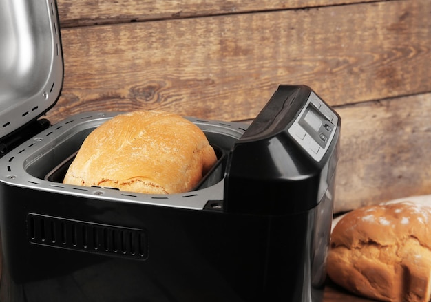 Freshly baked loaf in bread machine on wooden background