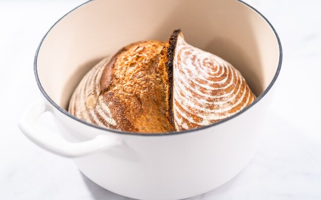 Свежеиспеченный хлеб на пшеничной закваске с отметками из корзины для расстойки хлеба в эмалированной чугунной голландской печи.