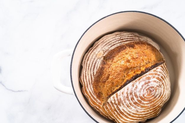 Freshly baked loaf of a wheat sourdough bread with marks from bread proofing basket in enameled cast iron dutch oven