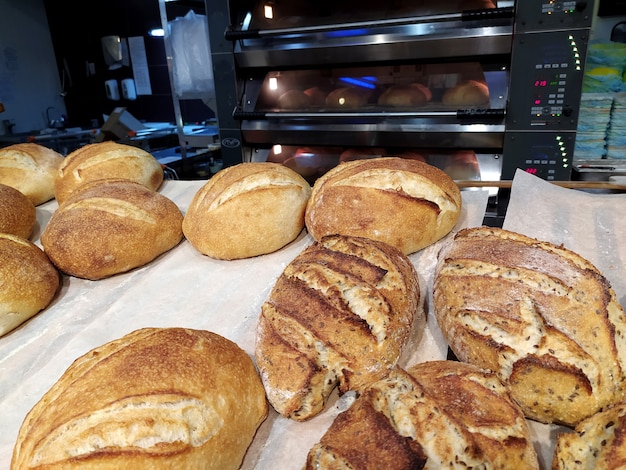 Freshly baked loaves of bread lie on a tray in a bakery, in the background there is a hot oven.