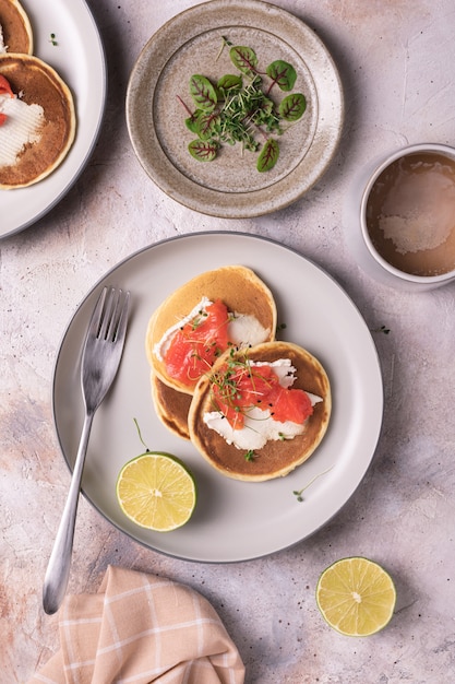 Freshly baked pancakes with salmon and microgreens on plates flat lay