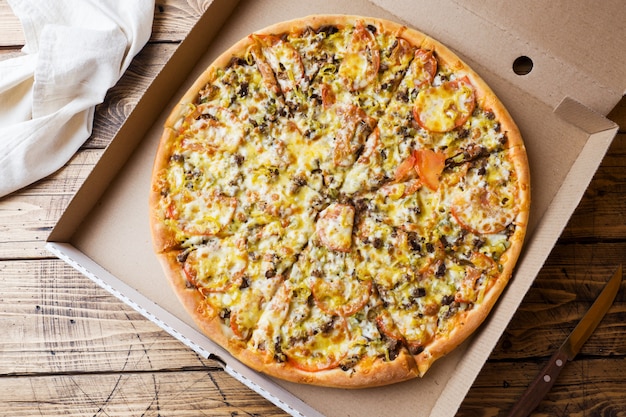 Freshly baked pizza in a cardboard box on a wooden table.