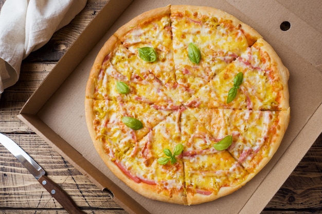 Freshly baked pizza in a cardboard box on a wooden table.