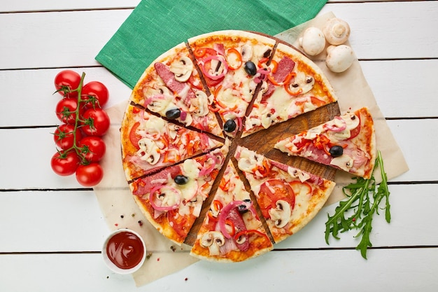 Freshly baked pizza with smoked sausages red pepper mushrooms onion and olives served on wooden background with tomatoes sauce and herbs Food delivery concept Restaurant menu Top view