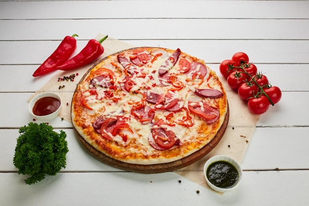 Pizza appena sfornata con salsicce affumicate peperoncino e pomodori serviti su sfondo di legno con salsa ed erbe concetto di consegna del cibo menu del ristorante