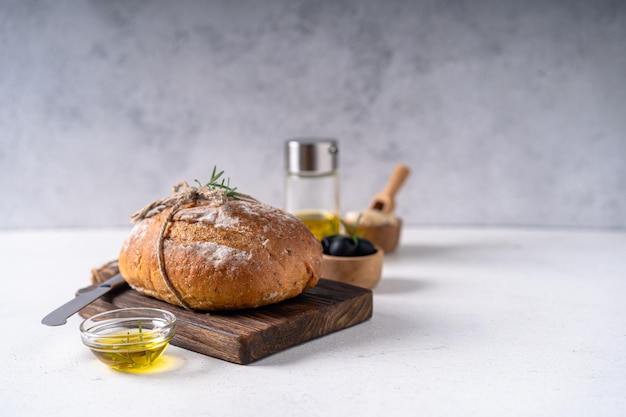 Freshly baked sourdough ciabatta artisan bread with olives and rosemary on a white abstract table