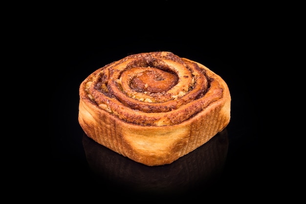 Freshly baked sweet bun with raisins and cinnamon isolated on black background. Homemade traditional bakery, baking bread and sweets concept.