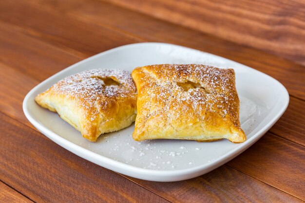 Freshly baked sweet buns sprinkled with powdered sugar and cinnamon on white plate on wooden table.