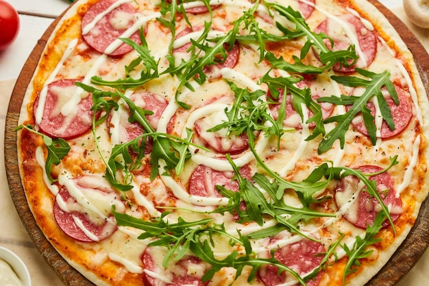 Freshly baked tasty pepperoni pizza with salami mozzarella cheese and rukkola served on wooden background with tomatoes sauce and herbs Food delivery concept Restaurant menu