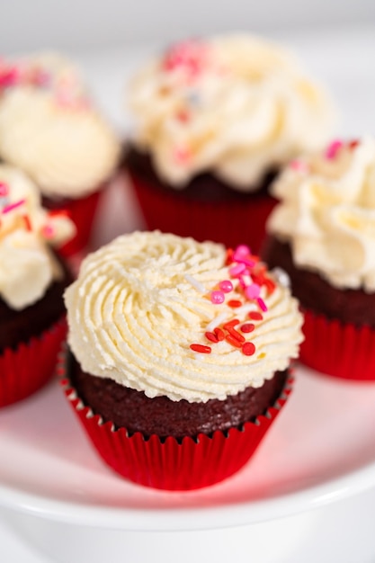 Freshly baked velvet cupcakes with white chocolate ganache frosting decorated with sprinkles