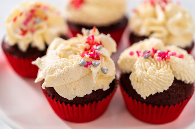 Freshly baked velvet cupcakes with white chocolate ganache frosting decorated with sprinkles