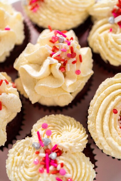 Freshly baked velvet cupcakes with white chocolate ganache frosting decorated with sprinkles