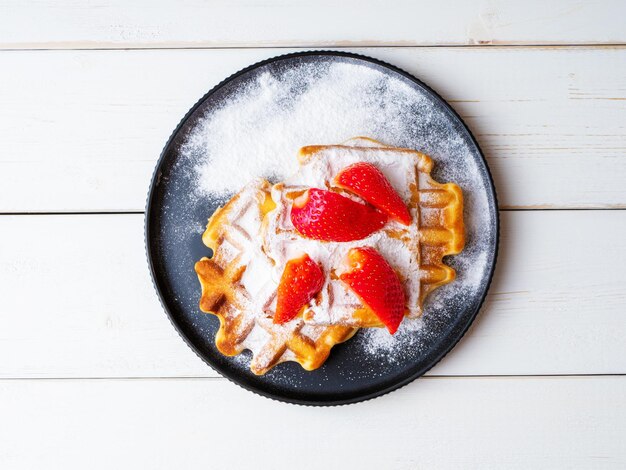 Photo freshly baked viennese waffles sprinkled with powdered sugar with strawberries