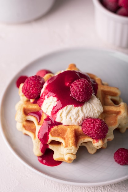 Freshly baked waffles with raspberry syrup and ice cream on a plate