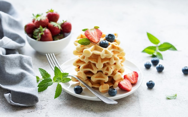 Photo freshly baked waffles with strawberries and blueberries on a concrete gray background