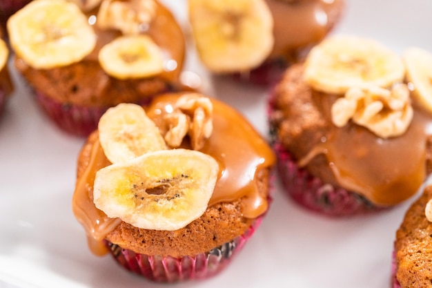 Freshly bakes banana nut bread muffins drizzled with homemade caramel, decorated with walnuts and banana chips.