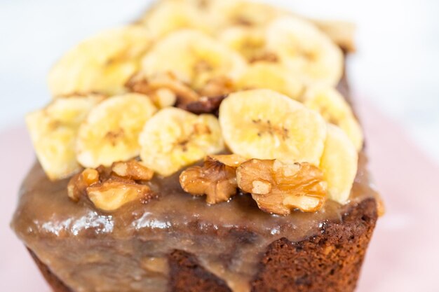 Freshly bakes a loaf of banana nut bread drizzled homemade caramel on a pink cutting board.