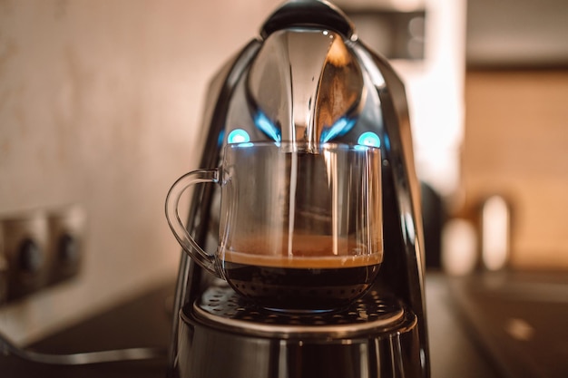 Freshly brewed coffee is poured from the coffee machine into glass cup in the kitchen at home