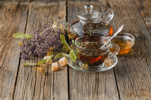 Фото Свежеприготовленный полезный чай с сушеной земляникой в стеклянном чайнике и чашкой на деревянном столе