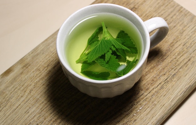 Freshly brewed melissa leaves in a cup on a wooden board