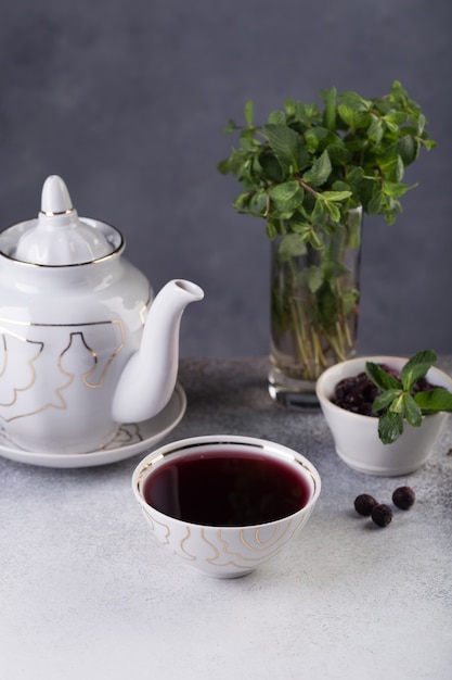 Freshly brewed tea is poured into a bowl, next to it is a chocolate cake decorated with a sprig of fresh herbs