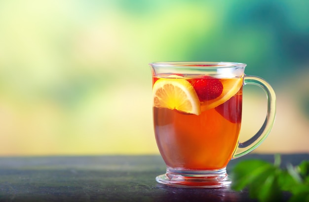 Foto tè appena preparato con limone e fragole in una grande tazza di vetro