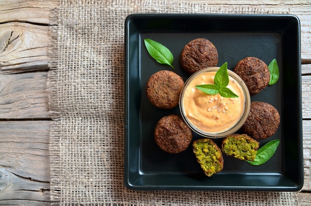 Freshly cooked falafel on a wooden table with tahini sauce.