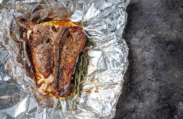 Freshly cooked juicy tbone steak with rosemary and garlic spices on a light marble background