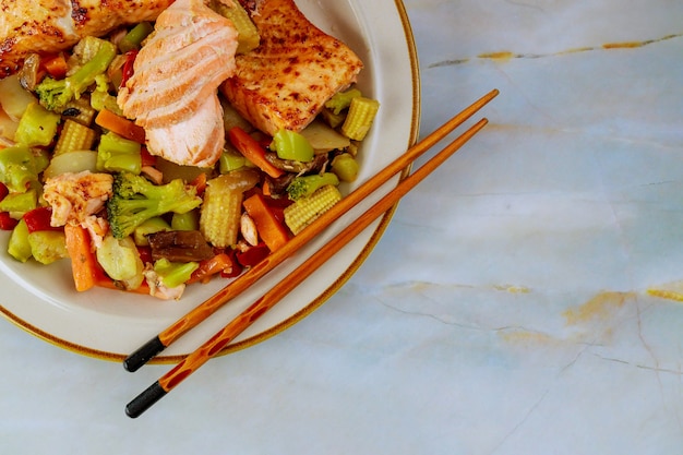 Freshly cooked salmon in plate with salad and lemon on white table.